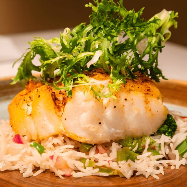 Pan-seared fish fillet with fresh greens, served over rice with vegetables at The Blue Taj.