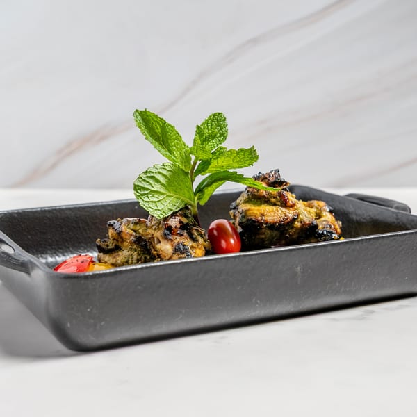 Indian chicken tikka with mint and cherry tomato in a black cast iron dish.