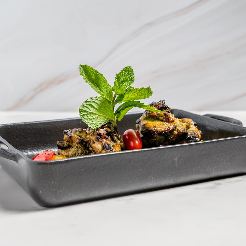 Indian chicken tikka with mint and cherry tomato in a black cast iron dish.