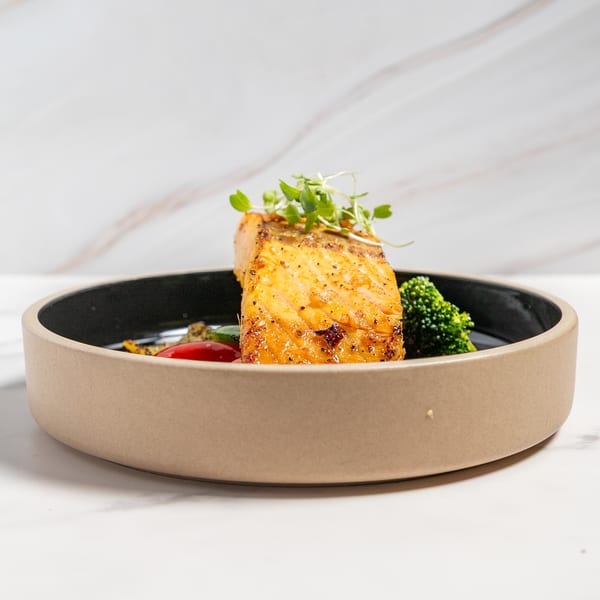 Golden-brown salmon fillet topped with microgreens, served with broccoli and red pepper in a bowl.