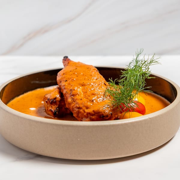 Indian chicken dish in a rich orange sauce, garnished with fresh dill and small tomatoes.