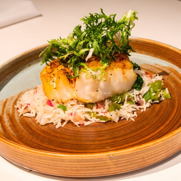 Pan-seared fish fillet with greens, rice, and vegetables on a rustic brown plate at The Blue Taj.